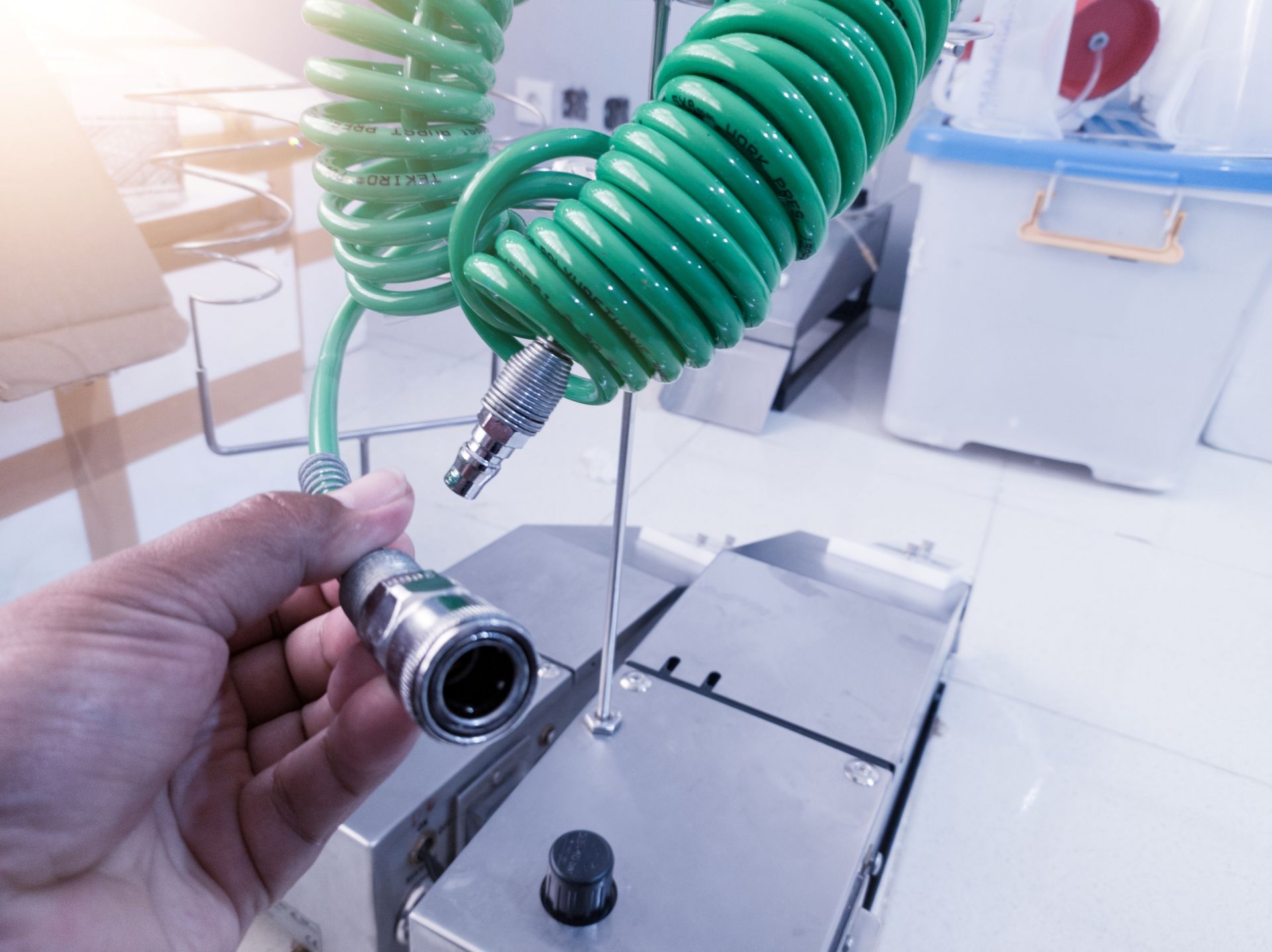 Schnellkupplung an grünem Spiralschlauch wird von Hand in Werkstatt angeschlossen